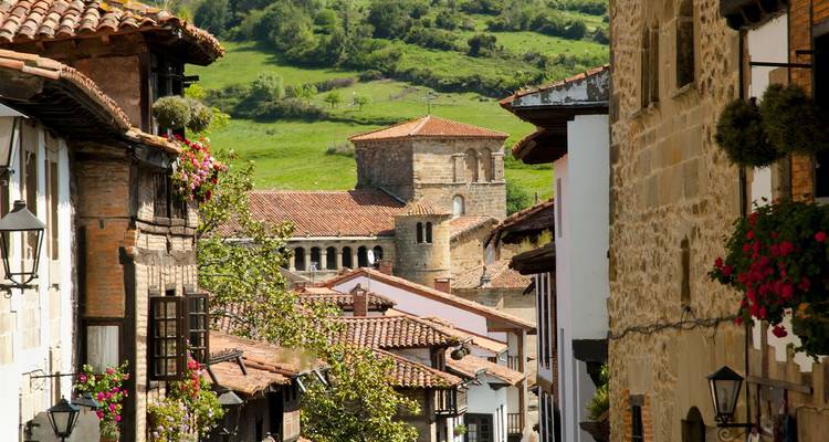 Encantadora calle empedrada con cestas de flores colgantes que domina una torre de iglesia de piedra en la rural Cantabria.