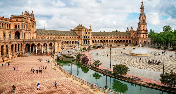 Vista amplia de la Plaza de España en Sevilla con turistas caminando por la plaza de azulejos y el canal