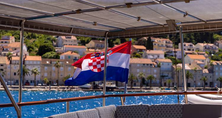 Croatian flag flying on a boat with a town in the background.