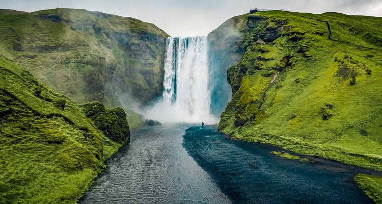 Large waterfall flowing into a river in a green landscape.