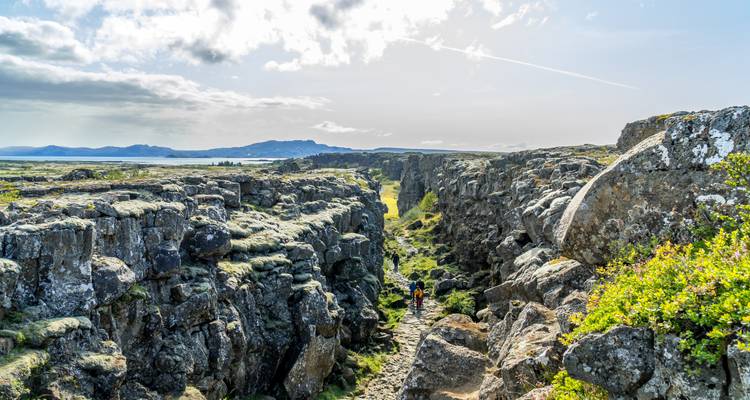 People walking along a rocky path through a rugged landscape.