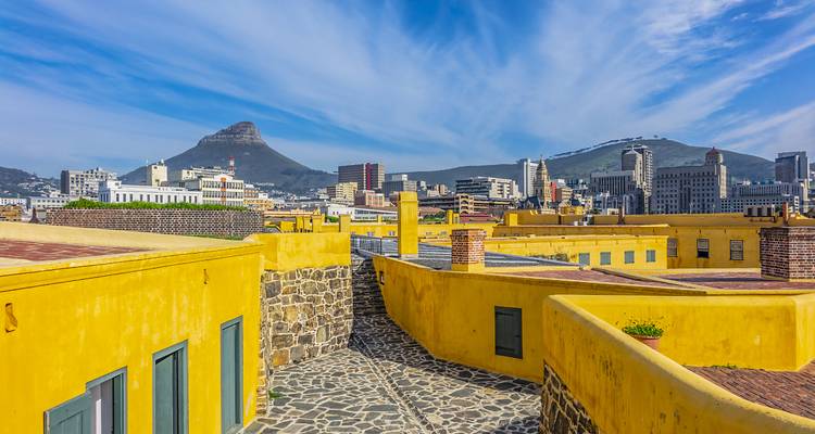 Farbenfrohe Dächer des Bo-Kaap-Viertels mit dem Lion's Head-Berg und der Skyline von Kapstadt unter streifigen blauen Wolken.