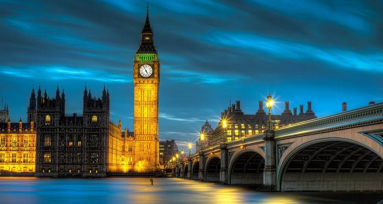 De verlichte Big Ben en het Parlementsgebouw naast de Westminster Bridge weerspiegeld in de Theems bij zonsondergang.