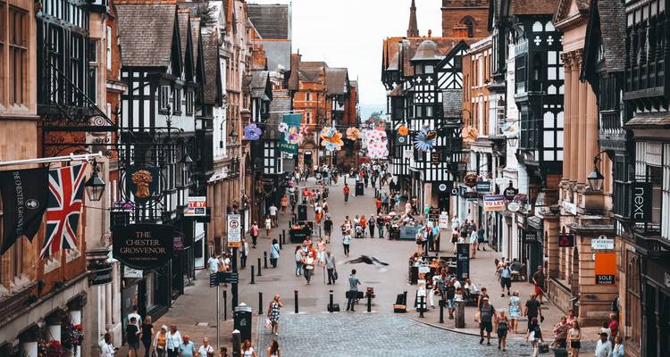 Drukke winkelstraat voor voetgangers in Chester met Tudor-achtige zwart-witte gebouwen en feestelijke slingers.