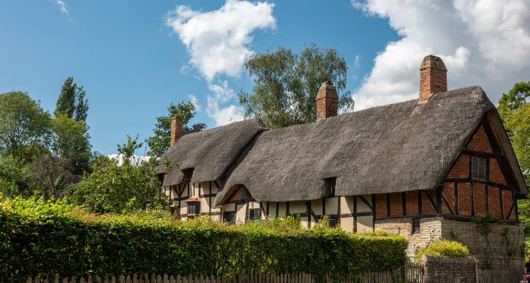 Schilderachtig rieten Tudor-huisje omgeven door groen onder een helderblauwe hemel in Stratford-upon-Avon.