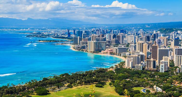 Aerial view of a coastline with a city skyline and mountains.