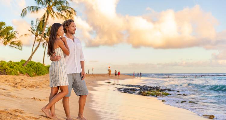 A couple walking along a sandy beach under a cloudy sky.