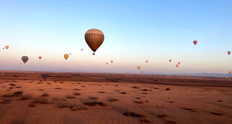 Plusieurs montgolfières volant au-dessus d'un paysage désertique au lever du soleil.