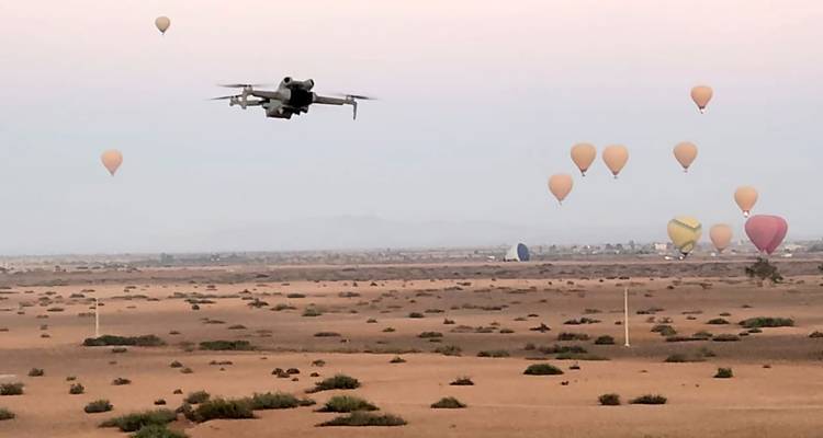 Un drone volant avec des montgolfières au loin au-dessus d'un désert.