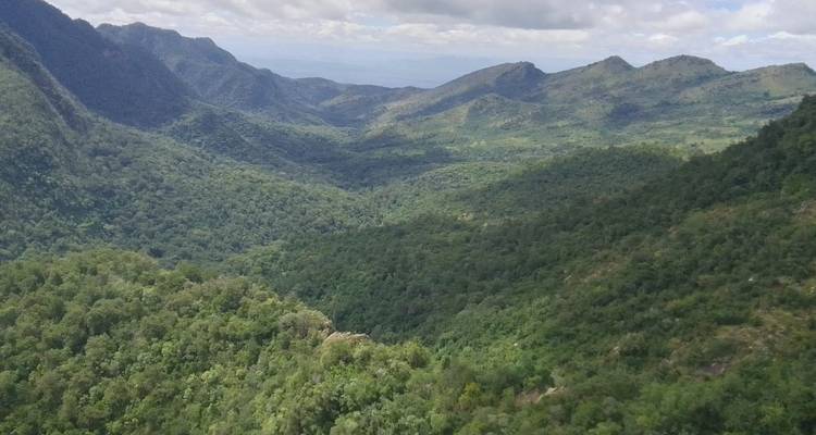 Vallée verdoyante luxuriante avec des collines environnantes sous un ciel partiellement nuageux.