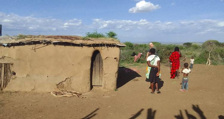 Maison traditionnelle en terre dans un cadre rural avec des personnes à l'extérieur.