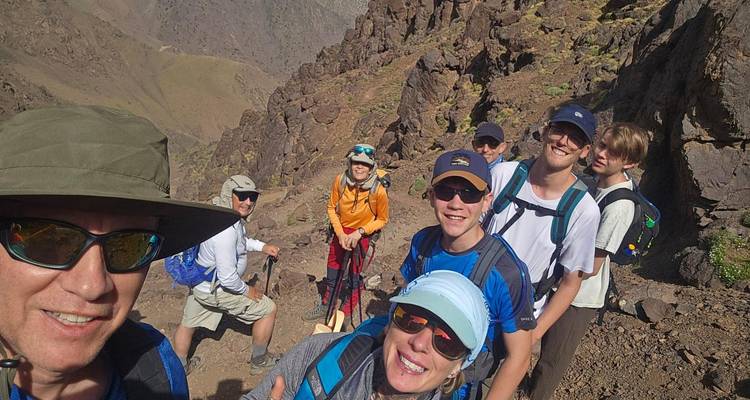 Un groupe joyeux de randonneurs prend un selfie sur un sentier de montagne rocheux en plein soleil.