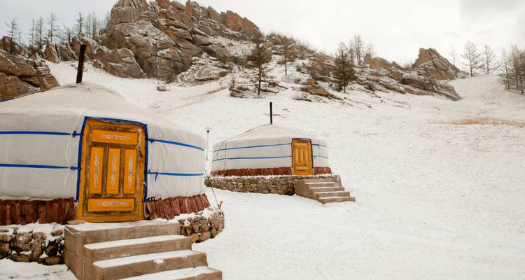 Yurtas tradicionales en un paisaje nevado junto a una colina rocosa.