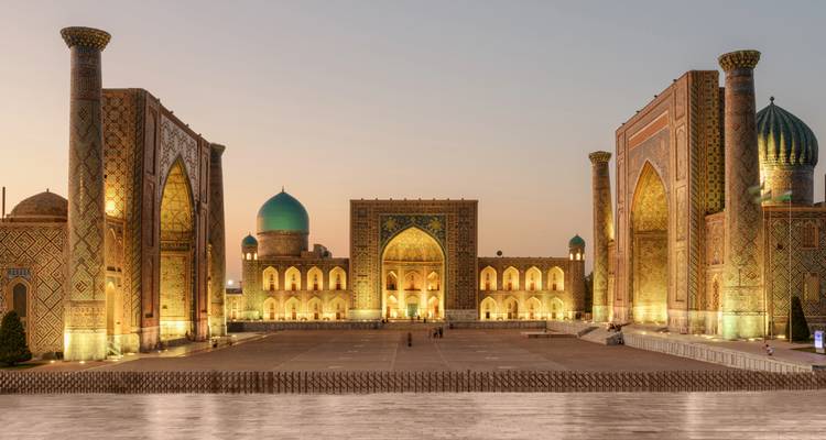 Les madrasas illuminées de la place du Régistan à Samarcande brillent chaleureusement au coucher du soleil, encadrant la vaste place historique.