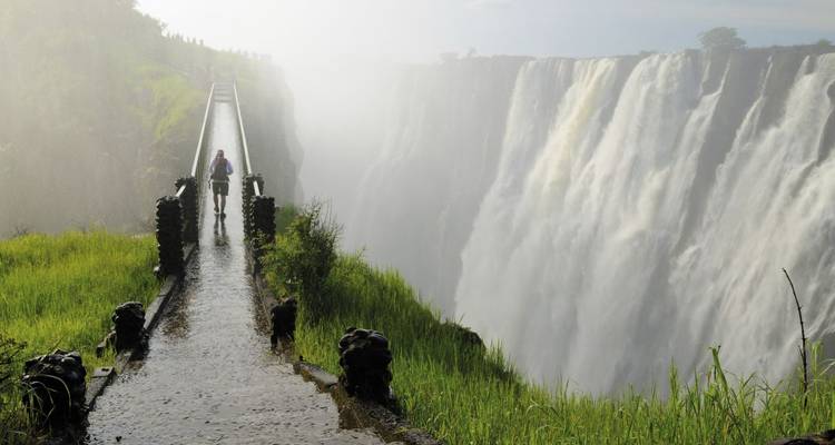 Puente cerca de una cascada con neblina, con una persona caminando.