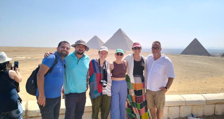 Group posing with Giza pyramids in the background on a sunny day.