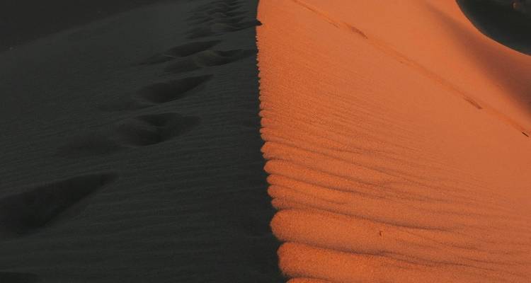 Footprints on a sand dune with a sunset glow.