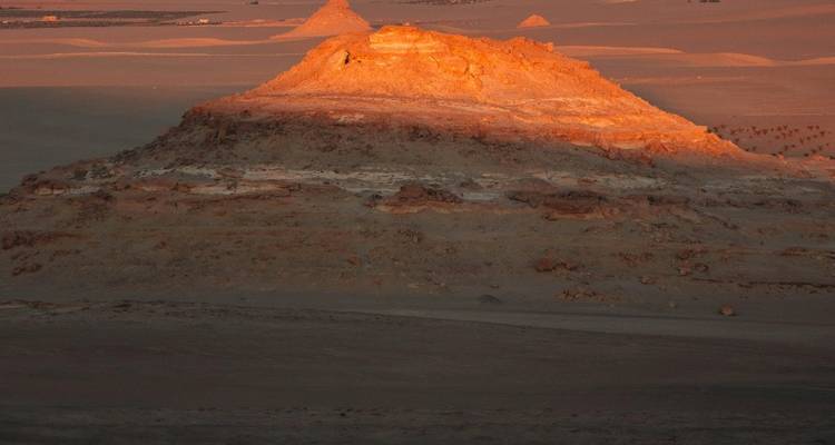 Sun setting over a rocky hill in a desert landscape.