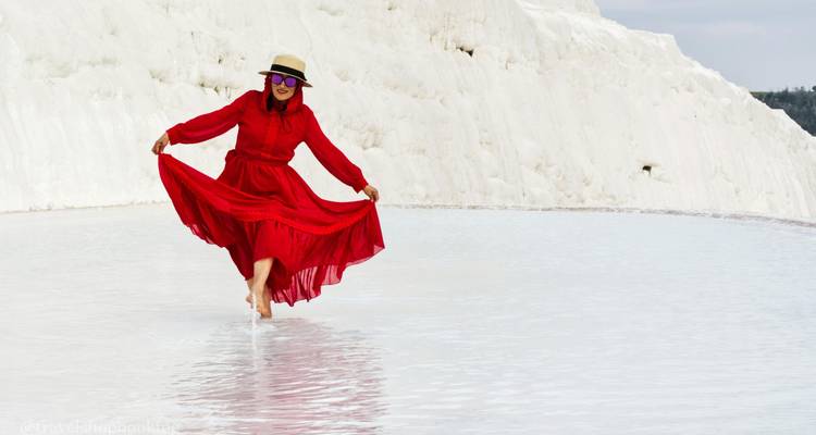Femme en robe rouge fluide marche joyeusement pieds nus dans un bassin thermal peu profond sur les terrasses blanches de Pamukkale