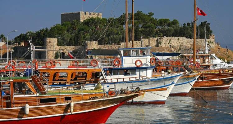 Boten in een haven met een oud fort op de achtergrond.