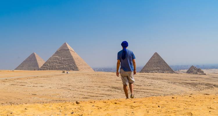 Solo-reiziger die over het woestijnplateau naar de drie Piramides van Giza loopt onder een heldere hemel.