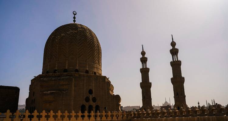 Silhouetten van historische koepels en slanke minaretten die zich aftekenen tegen een mistige heldere lucht boven Caïro.