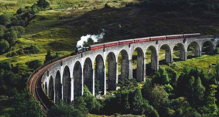 Train à vapeur traversant le viaduc de Glenfinnan dans un paysage luxuriant.