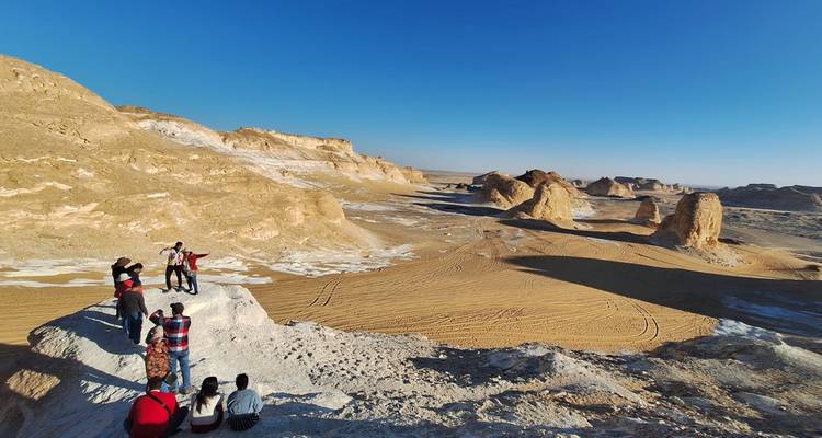 Les voyageurs se tiennent au sommet d'une crête calcaire surplombant un vaste bassin sablonneux rempli de formations sculptées par le vent dans le Désert Blanc.