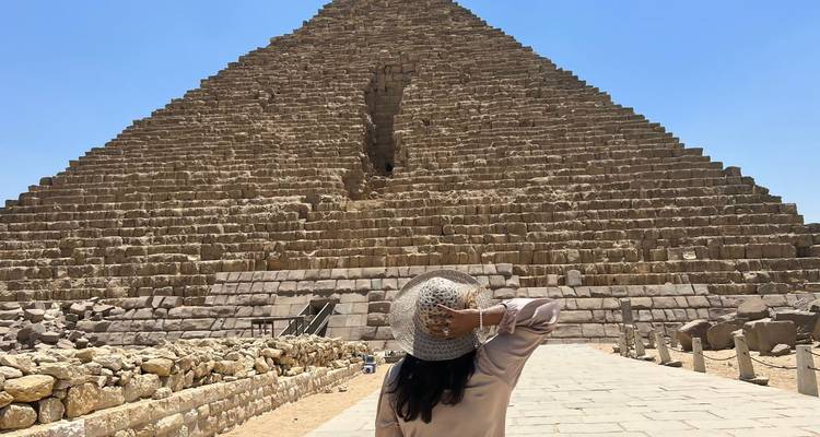 Tournant le dos à l'appareil photo, un visiteur admire les imposants blocs de calcaire de la Grande Pyramide depuis sa base.