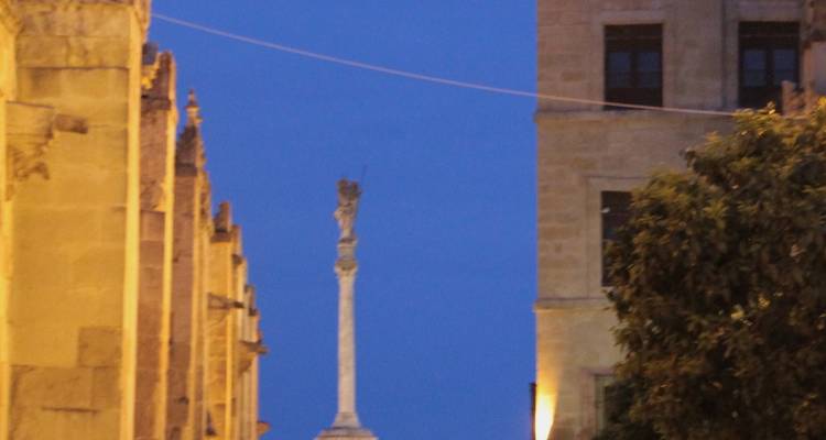 Blurry image of a column with surrounding buildings at night.