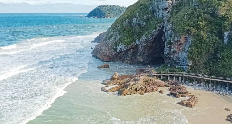 Rotsachtige kust met een zeegrottes en turquoise golven die op een zandstrand spoelen.