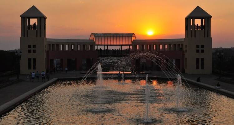 Zonsondergang die warm licht over een vijver en fonteinen werpt met een gesilhouetteerd paviljoen.