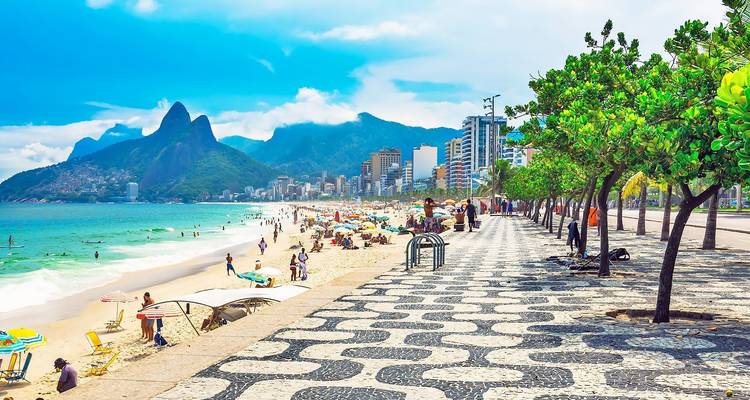 Levendige Ipanema strandpromenade met gemustereerde bestrating, zonnebaders, turquoise zee en de Dois Irmãos pieken.