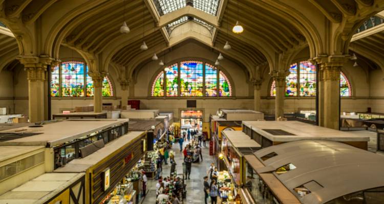 Druk interieur van São Paulo's Mercado Municipal met kleurrijke glas-in-loodramen en voedselkraampjes.