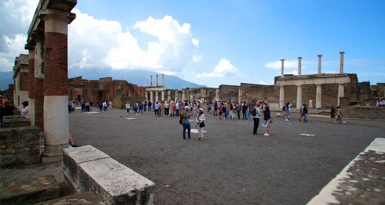 People gathered in a large open area in Pompeii, with ancient columns and ruins.