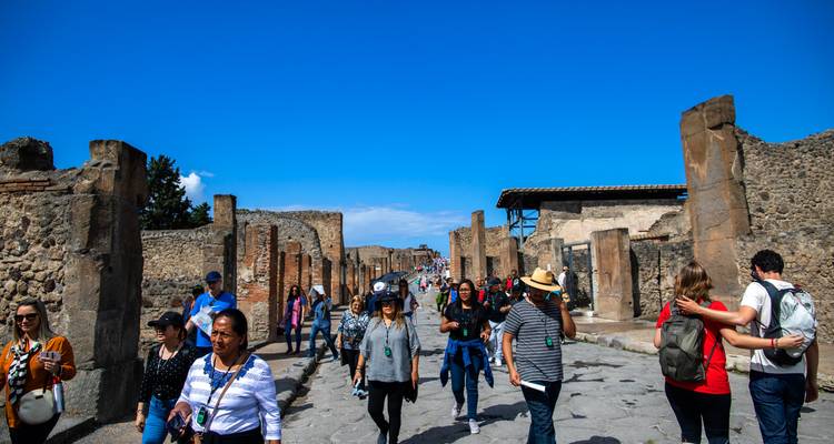 Tourists exploring the ancient street of Pompeii with ruins on either side.