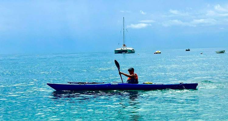 Person kayaking in the ocean with boats in the background.