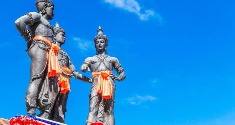 Trois statues de bronze avec des écharpes orange contre un ciel bleu.