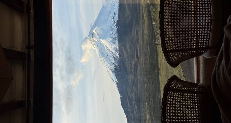 Vista de una montaña cubierta de nieve a través de una ventana con dos sillas.