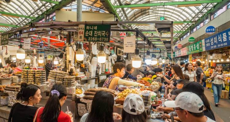 Mercado concurrido con gente comprando y puestos vendiendo mercancías.