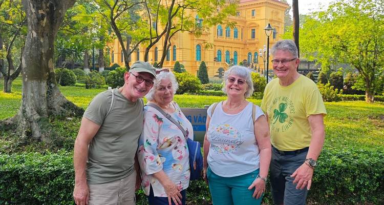Vier Personen lächeln in einer Gartenumgebung mit einem historischen Gebäude.