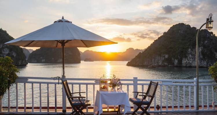 Romantisches Outdoor-Dining-Setup mit Blick auf die Halong-Bucht bei Sonnenuntergang.