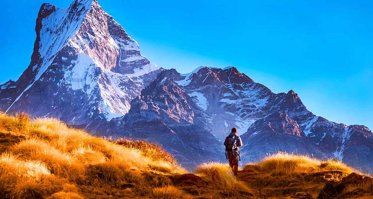 Person trekking on a trail with majestic snowy mountains in the background.