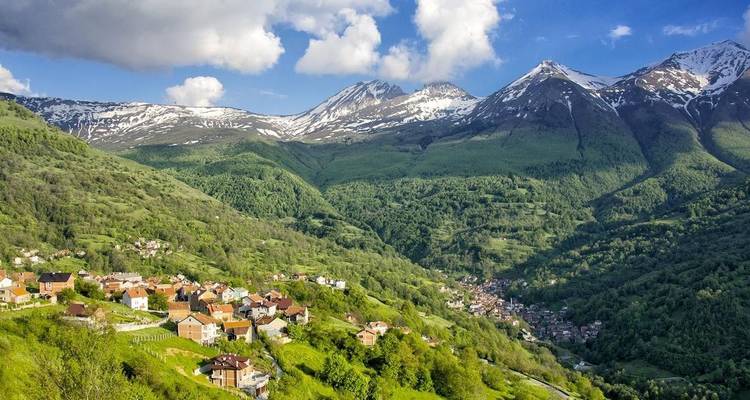 Un paysage pittoresque composé de montagnes aux sommets enneigés et d'une vallée parsemée de maisons.