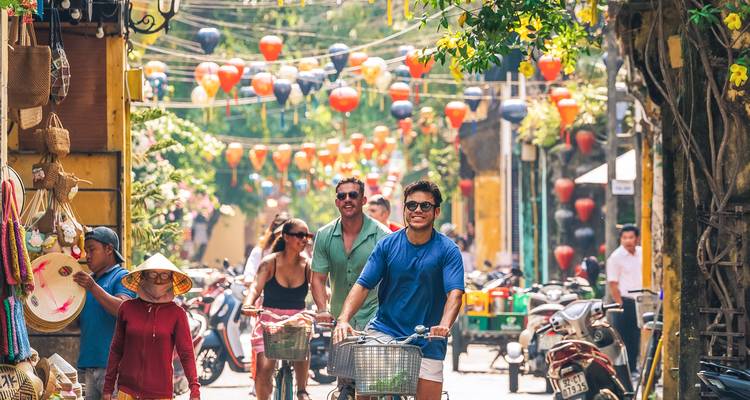 Rue animée bordée de lanternes à Hoi An avec des touristes à vélo et à pied.