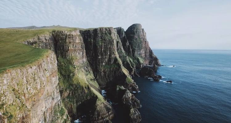Dramatic cliffs over an ocean under a clear blue sky.
