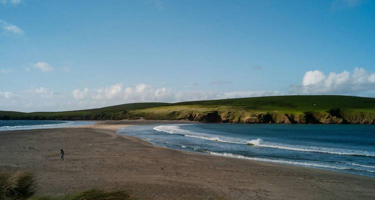A remote beach with waves and grassy hills.