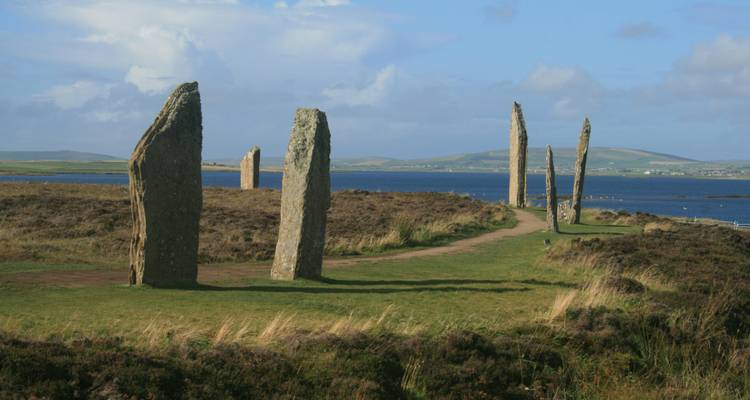 Standing stones forming a circle on a grassy plain by the sea.