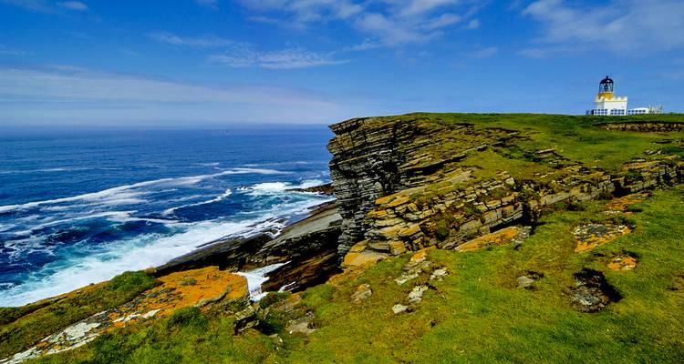 A cliff with a lighthouse overlooking rough ocean waves.