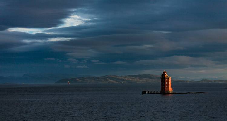 Phare rouge solitaire sur un petit affleurement rocheux sous un ciel nuageux dramatique